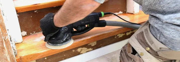 Person schleift Holztreppe mit Schleifmaschine